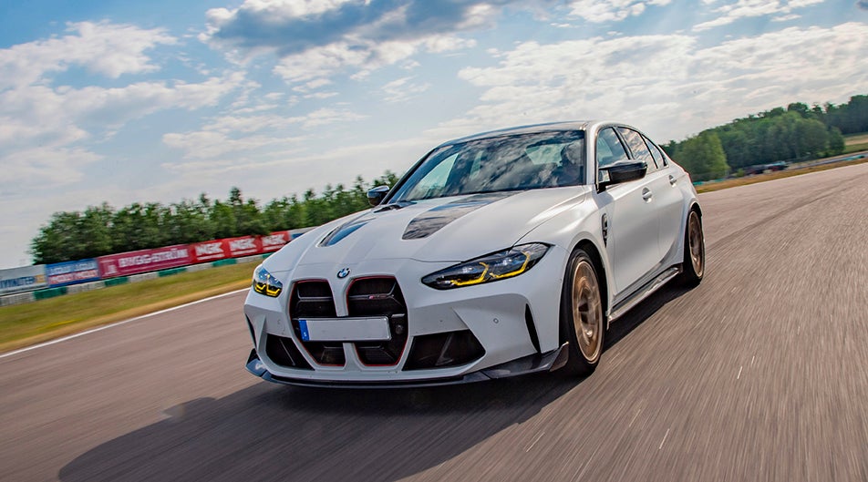 White BMW M3 G80 equipped with Öhlins suspension driving fast on a racetrack.